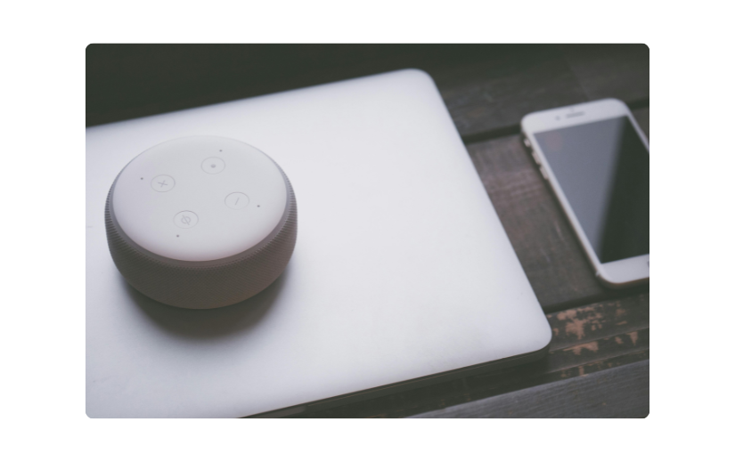 Altavoz inteligente en una computadora portátil junto a un teléfono inteligente, ideal para la promoción de productos de Amazon de dispositivos tecnológicos.